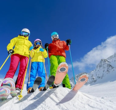 Tineri cu echipamente de ski colorate, pe partie, cu muntele inzapezit pe fundal