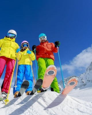 Tineri cu echipamente de ski colorate, pe partie, cu muntele inzapezit pe fundal
